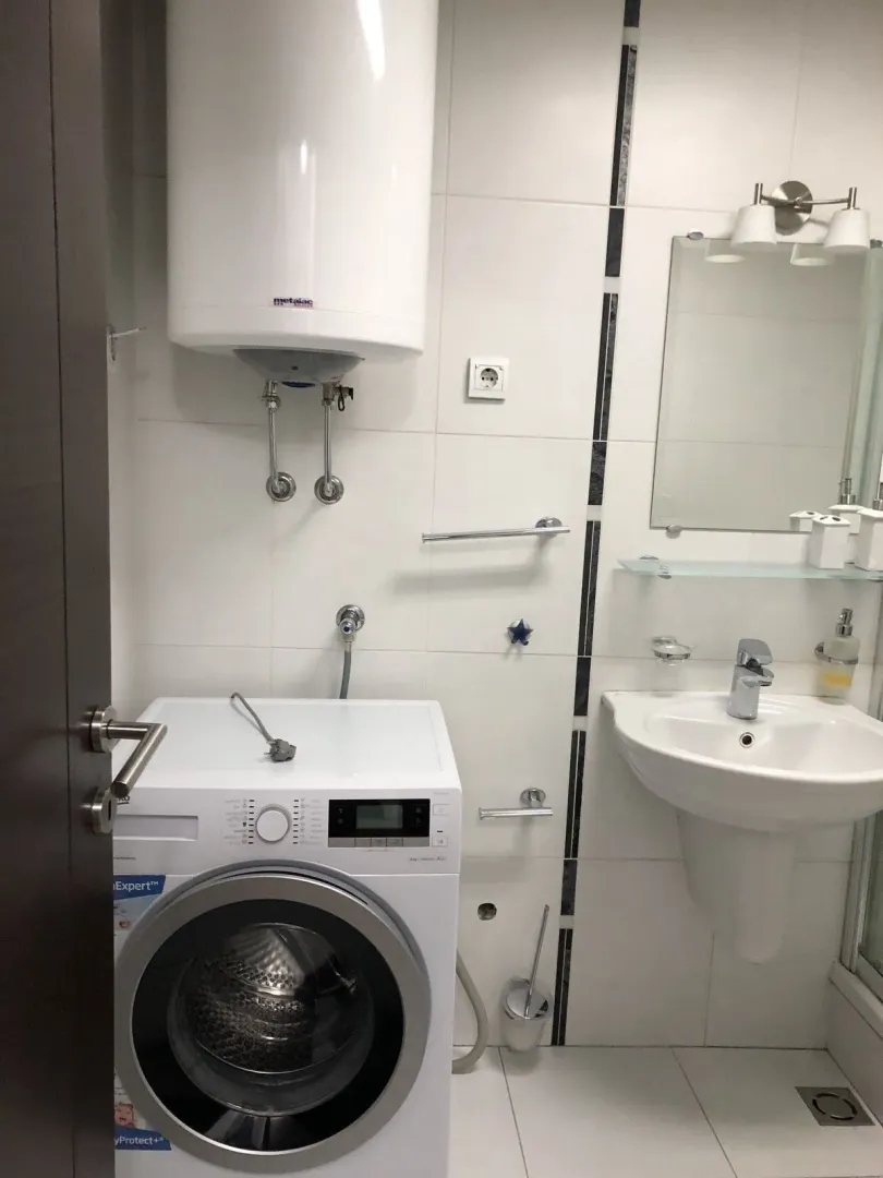 A bright bathroom featuring a washing machine, water heater, and sink.