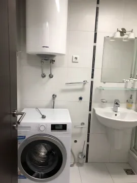 A bright bathroom featuring a washing machine, water heater, and sink. - image 20