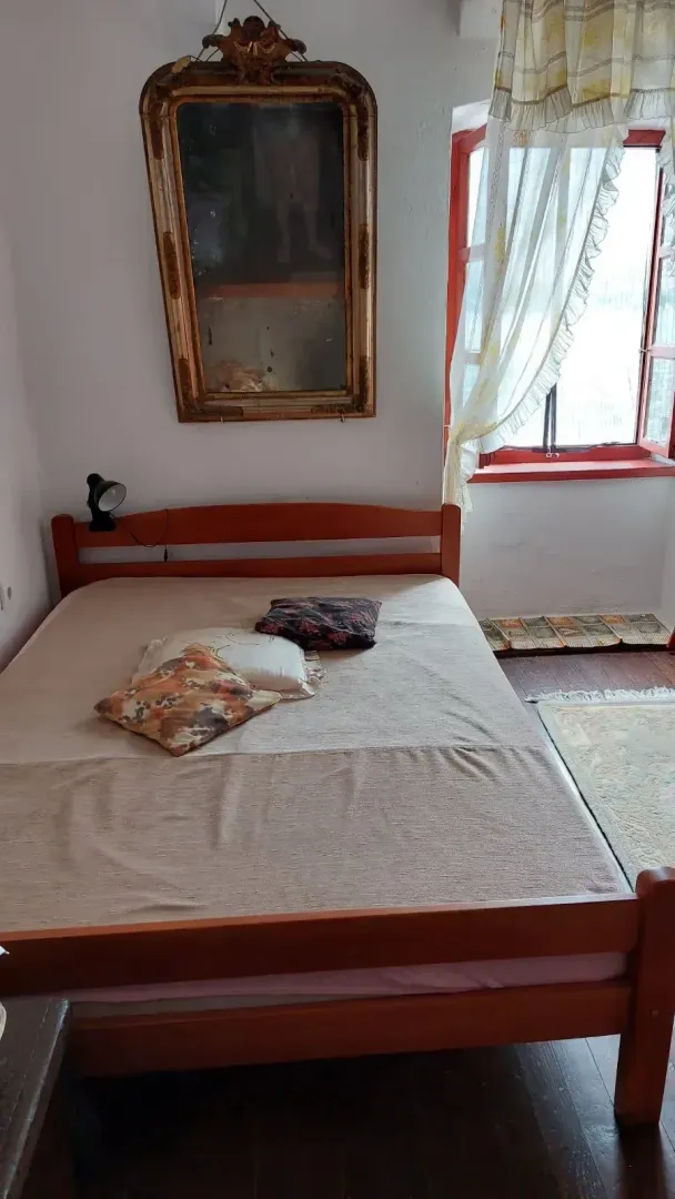 Spavaća soba sa drvenim krevetom, prozorom i ogledalom na zidu.