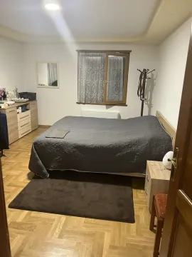 A simply furnished bedroom featuring a double bed, parquet flooring, and wooden furniture. - image 21