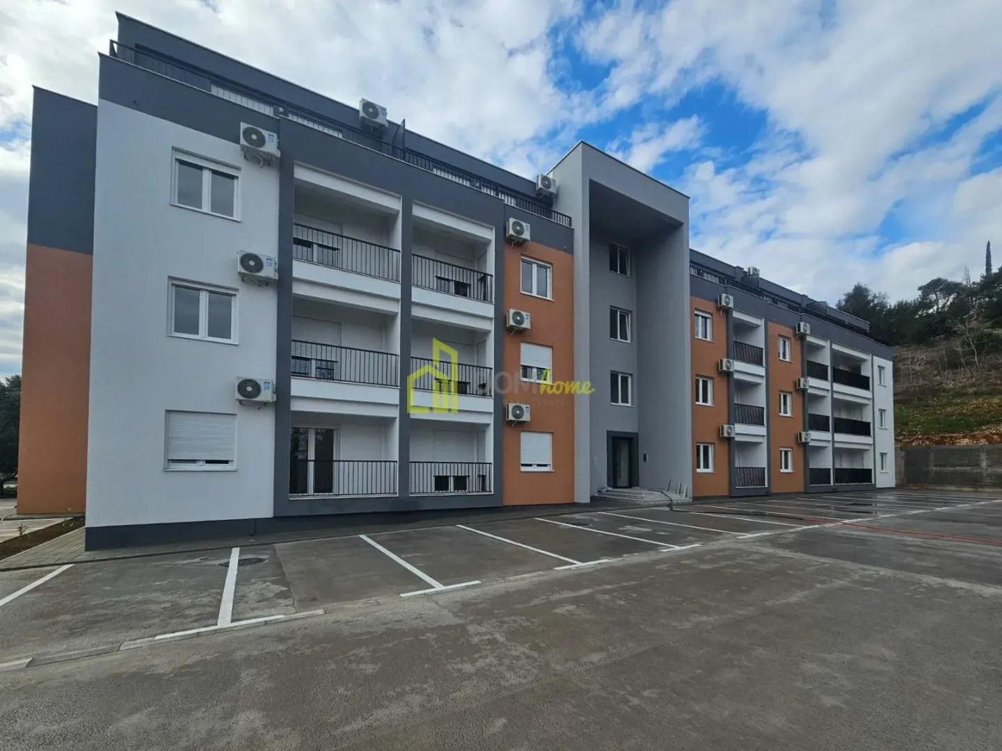 Spoljašnji izgled stambene zgrade sa parkingom ispred.