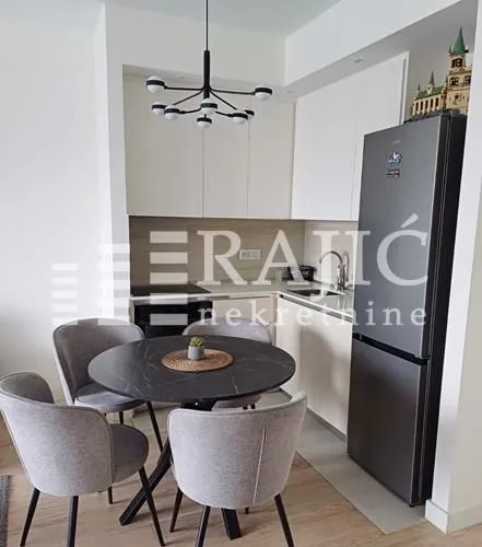 Dining area with a modern table and chairs and a kitchen in the background.