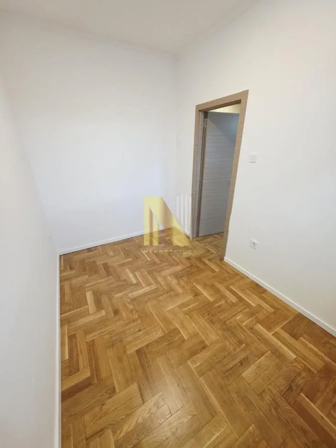 Prazna soba sa parketom i belim zidovima.