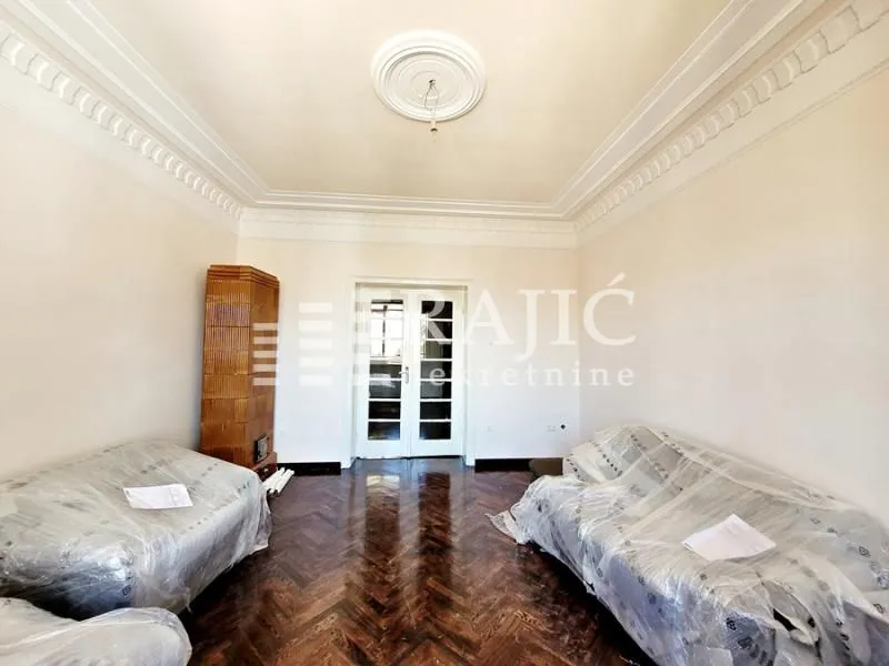 Spacious living room with parquet flooring and furniture covered with protective wrap.