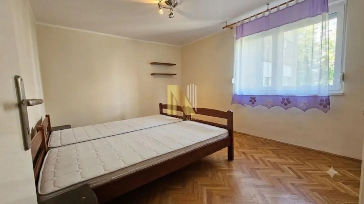 Spavaća soba sa bračnim krevetom i prozorom sa zavesama.