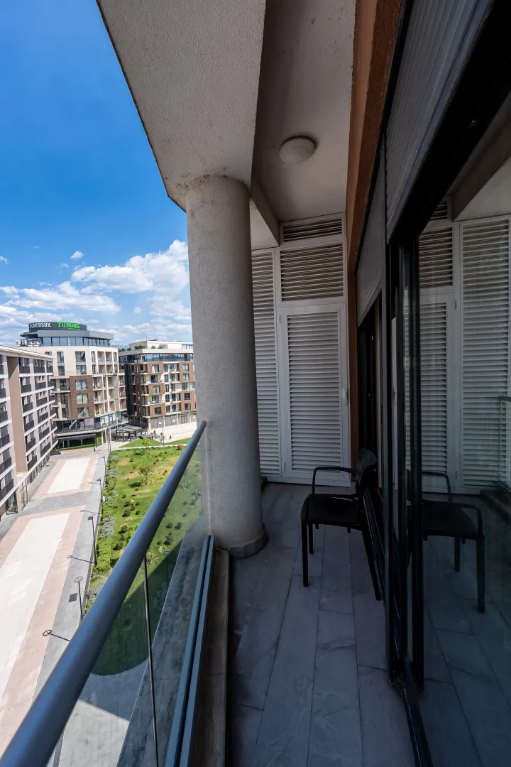 Covered balcony with glass railing and a view of the neighborhood and courtyard.