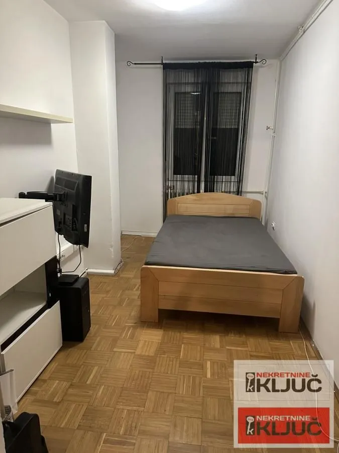 Nameštena spavaća soba sa bračnim krevetom i drvenim parketom.