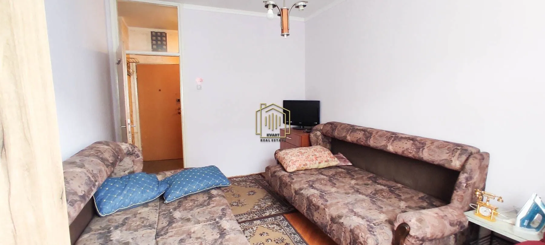 Living room with two sofas, a television, and a view towards the entrance door.