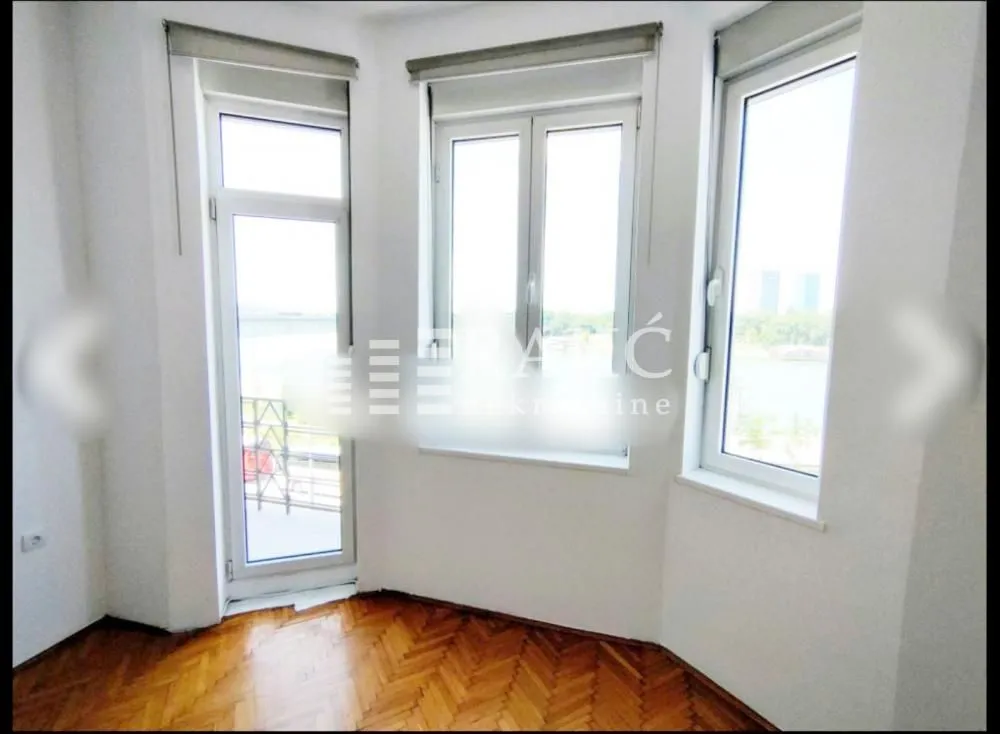 Empty room with hardwood floors and large windows.