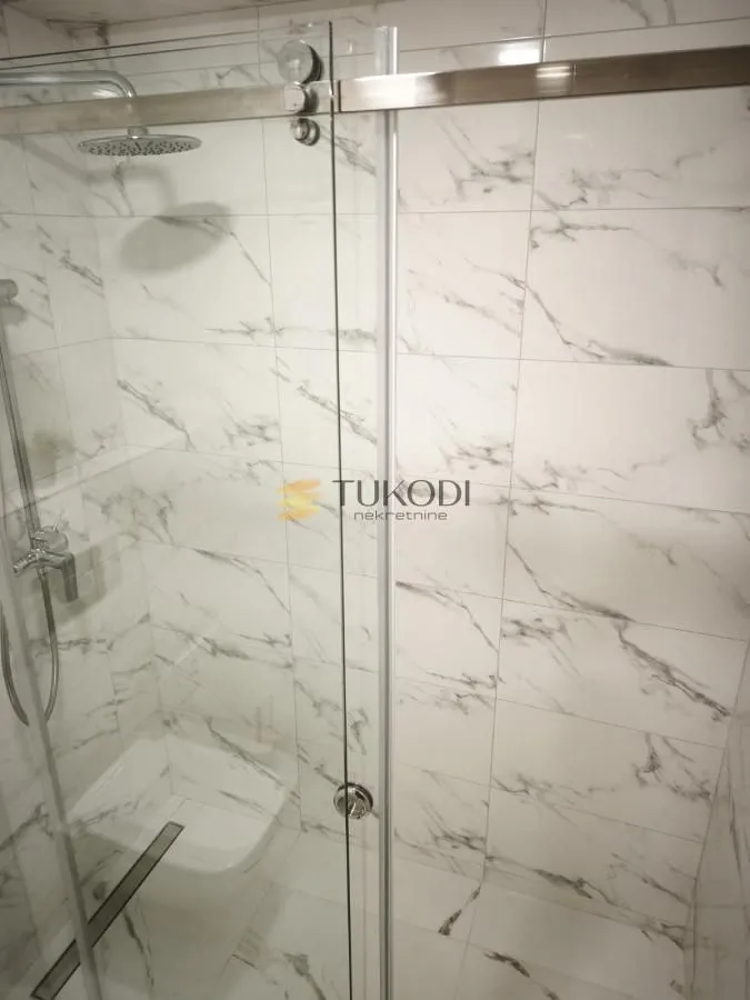 Walk-in shower with marble-look tiles and a glass screen.