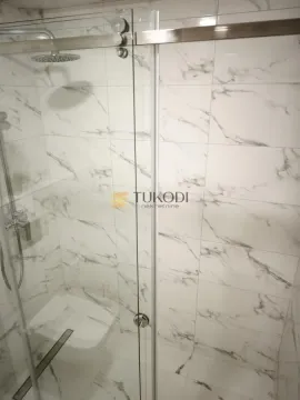 Walk-in shower with marble-look tiles and a glass screen. - image 5