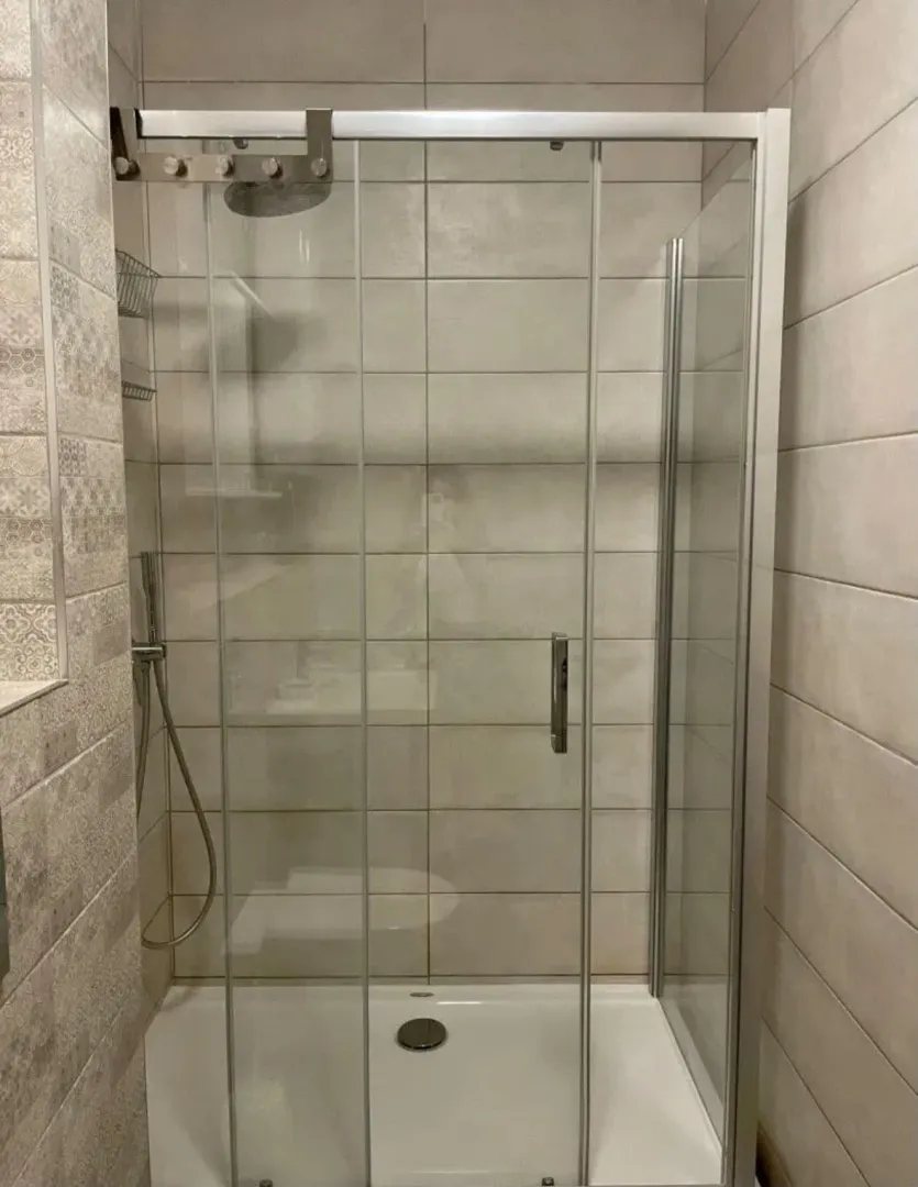 Moderna tuš kabina sa staklenim paravanom i keramičkim pločicama na zidu.
