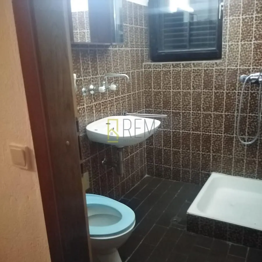 Manje kupatilo sa tuš kabinom obloženo tamnim keramičkim pločicama.
