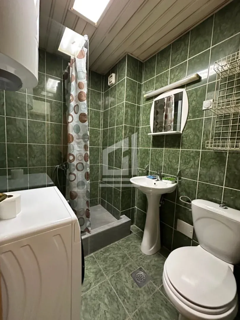 Kupatilo sa zelenim pločicama, umivaonikom, WC šoljom i tuš kabinom.