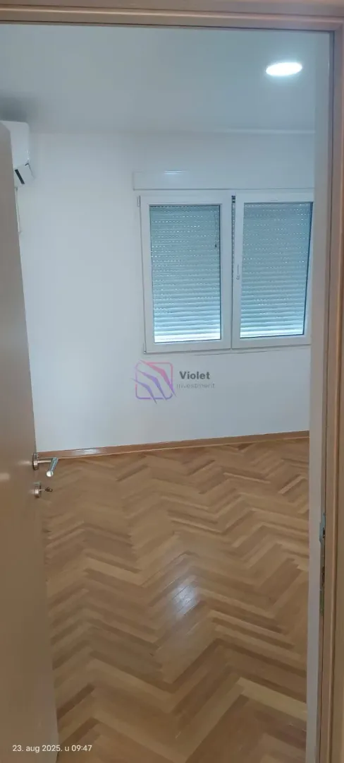 An empty room with wooden parquet flooring and a window viewed from the doorway.