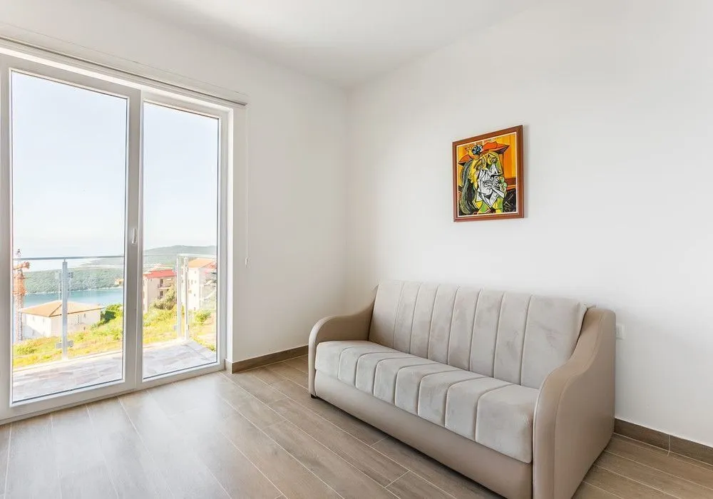 Svijetla prostorija sa modernim kaučem i izlazom na balkon sa pogledom.