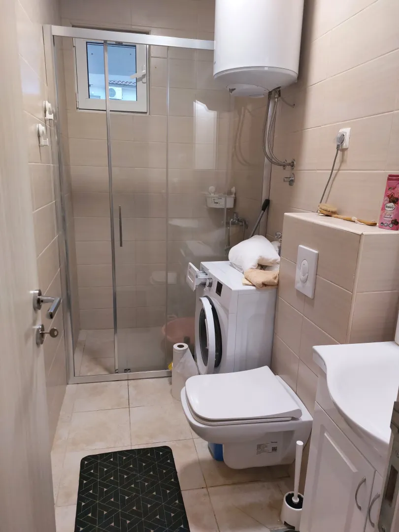 Smaller bathroom with a shower cabin, toilet, and washing machine.