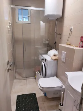 Smaller bathroom with a shower cabin, toilet, and washing machine. - image 13