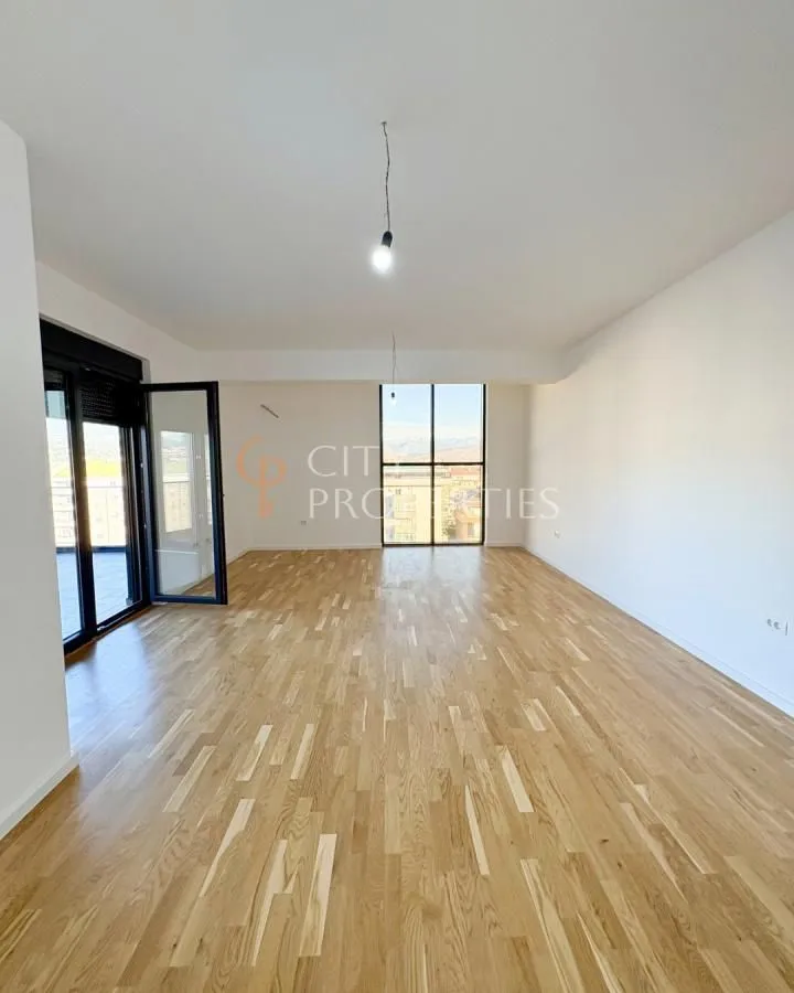 Spacious empty room with wooden flooring and large windows.