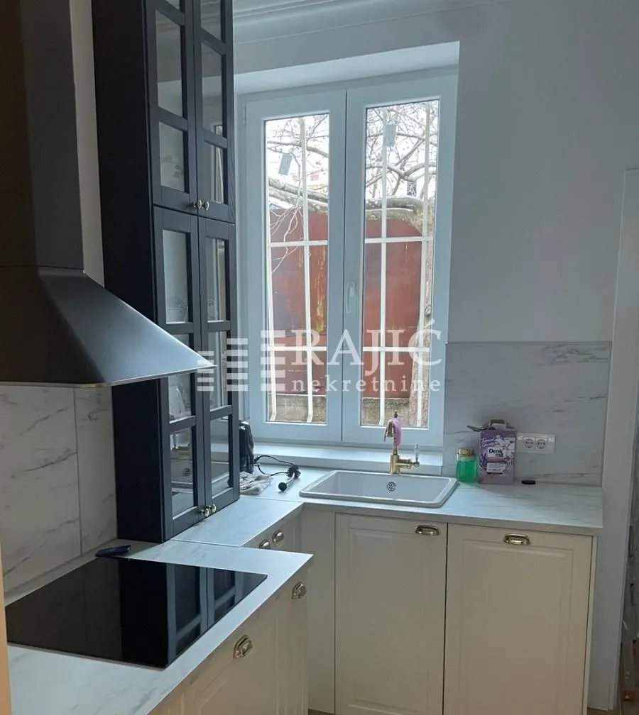Compact kitchen with a sink, built-in cooktop, and upper cabinets next to the window.