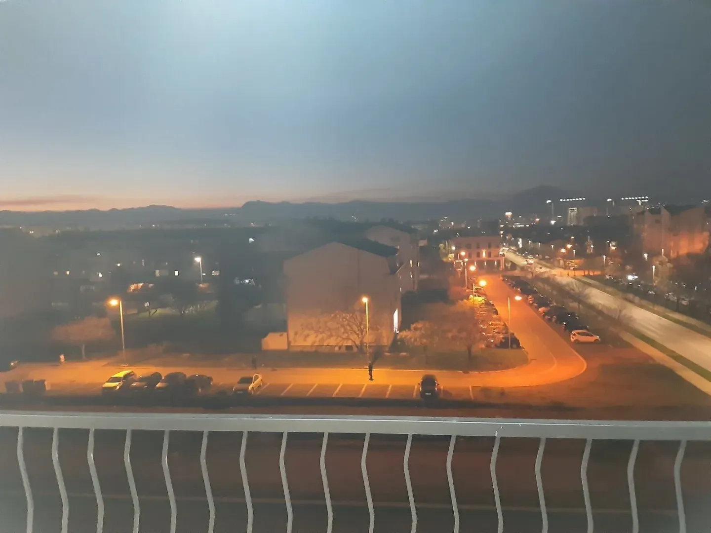 Evening view from the balcony overlooking illuminated streets and nearby buildings.