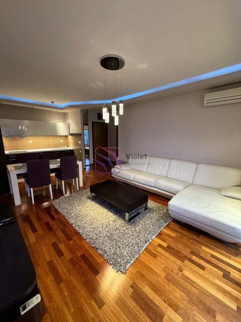 Living room with a sofa set, dining area, and kitchen in the background.