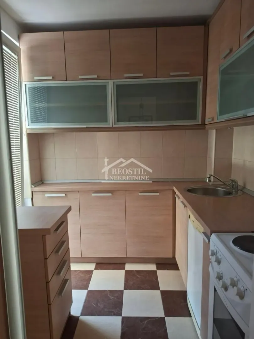 Manja kuhinja sa drvenim elementima i pločicama šahovskog uzorka na podu.