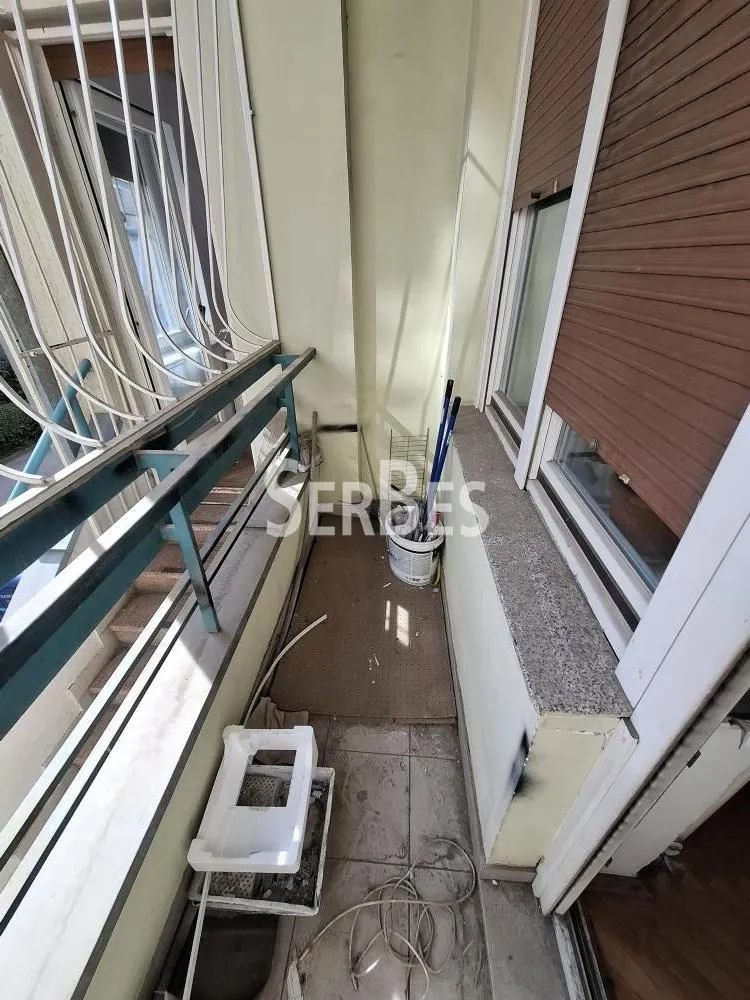 Manji nenamešten balkon sa metalnom ogradom i prozorima sa spoljnim roletnama.