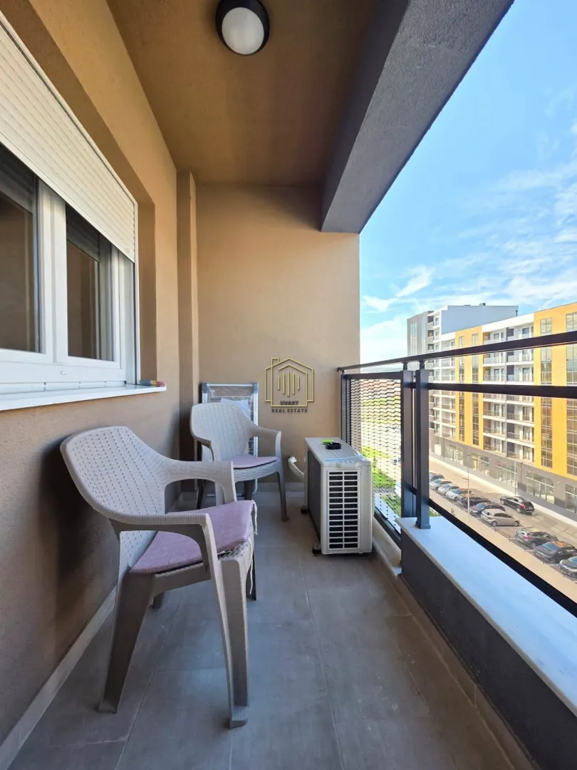 Natkriveni balkon sa garniturom za sjedenje i pogledom na okolne zgrade.