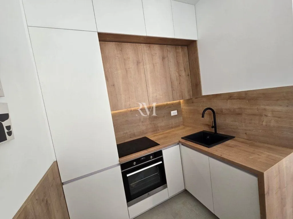 Modern kitchen with white cabinets, wooden surfaces and a built-in oven.