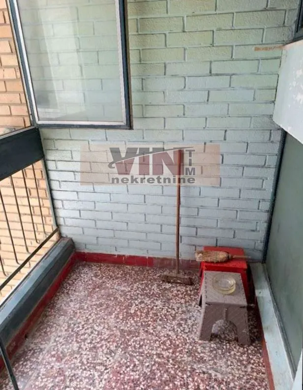 Manji zatvoreni balkonski prostor sa ciglenim zidom i metlom.