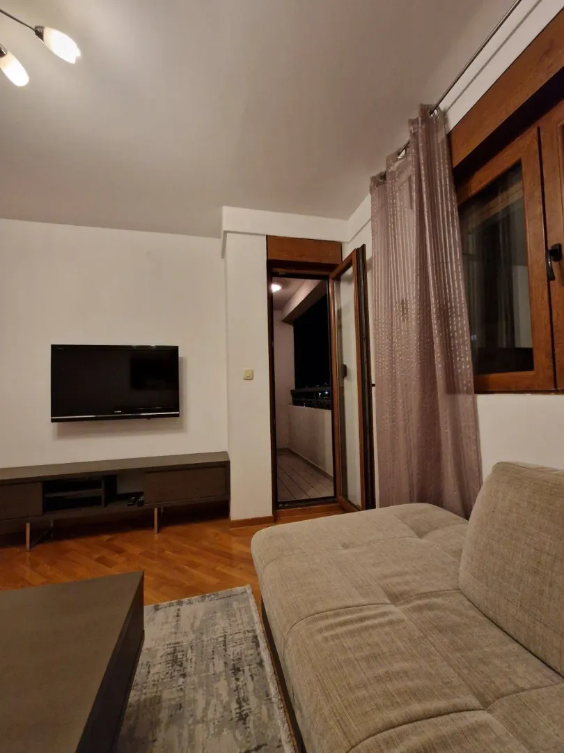Dnevna soba sa televizorom montiranim na zid i izlazom na balkon.