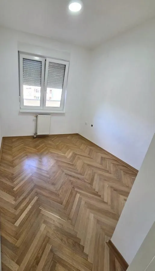 Prazna soba sa parketom i prozorom.