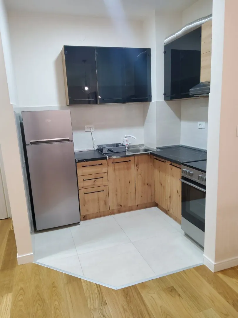 A small modern kitchen with wooden and black cabinets and a refrigerator.