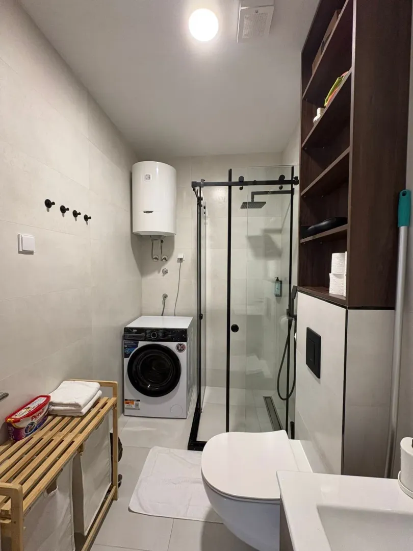 Modern bathroom with a walk-in shower, washing machine, and sanitary fixtures.