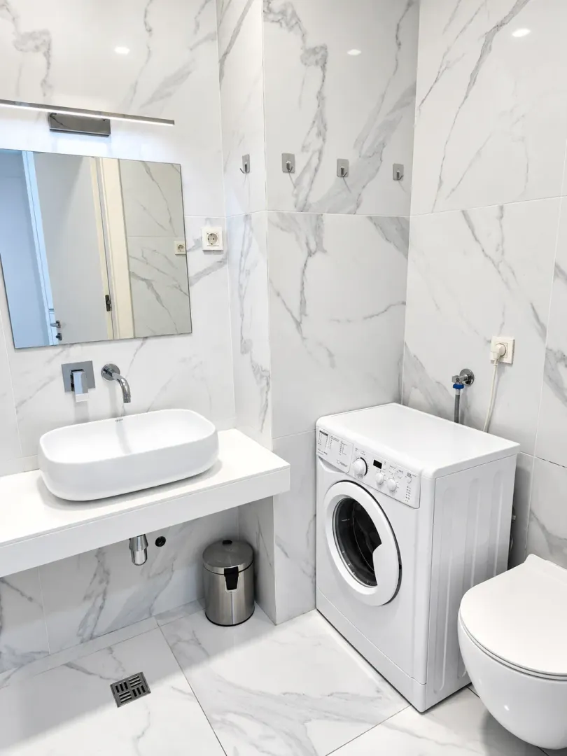 Modern bathroom with a sink, washing machine, and marble tiles.