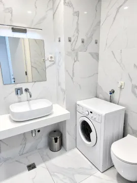 Modern bathroom with a sink, washing machine, and marble tiles. - image 10