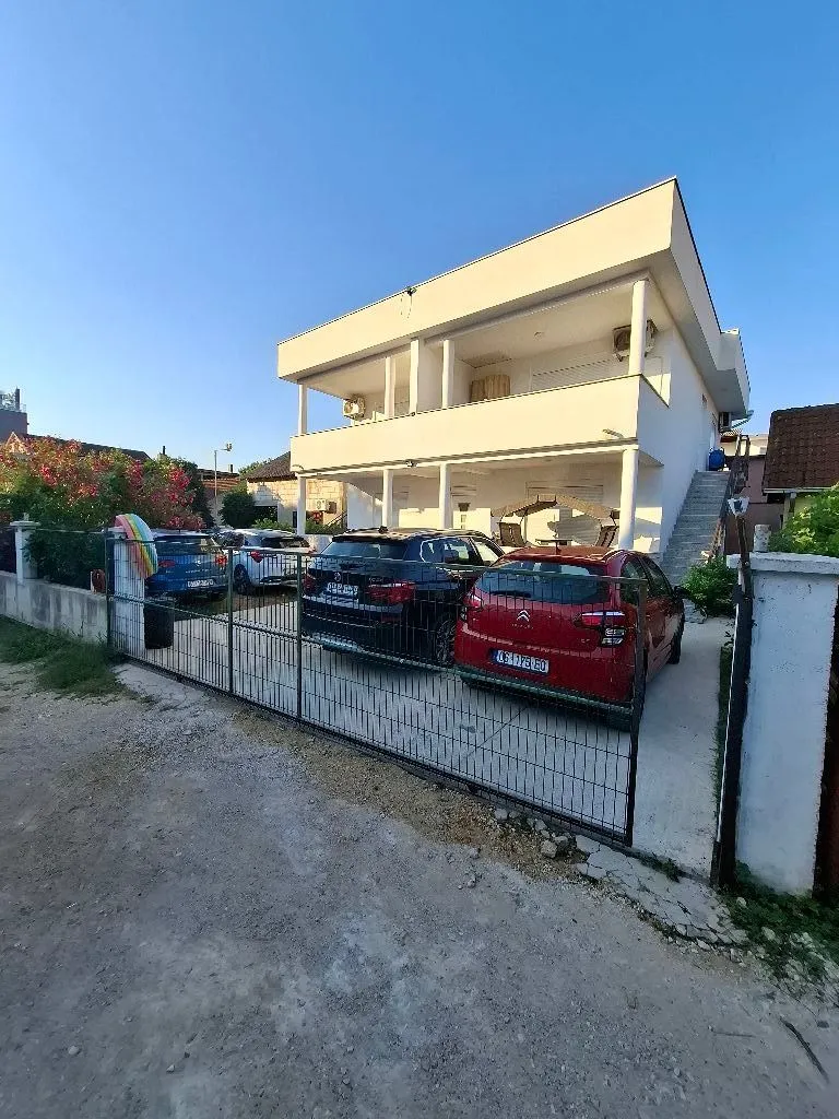 Eksterijer dvospratne bijele kuće sa dvorištem i parkiranim automobilima.