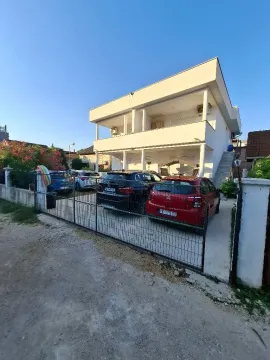 Eksterijer dvospratne bijele kuće sa dvorištem i parkiranim automobilima. - image 2