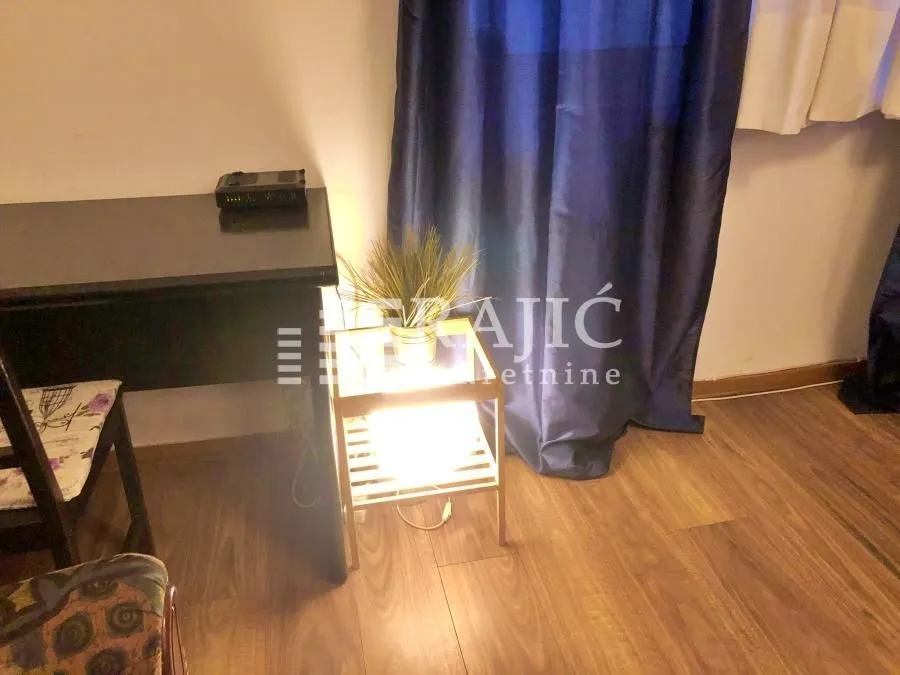 Part of a furnished room with a desk, shelf, and curtains.