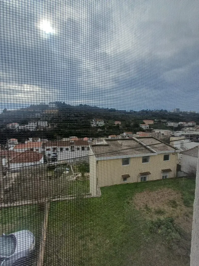 Pogled sa prozora na okolne zgrade i brdo.