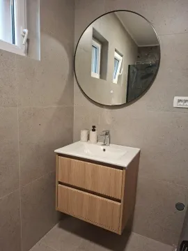 Bathroom with a vanity, wooden cabinet, and round mirror. - image 11