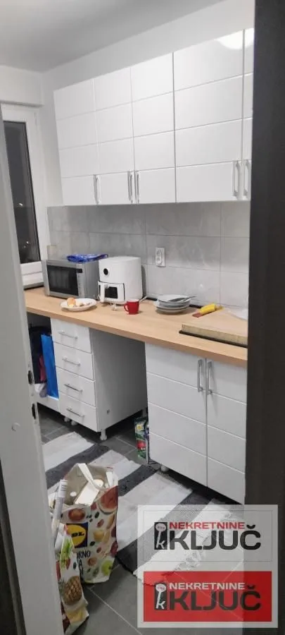 Pogled na manju kuhinju sa belim elementima i drvenom radnom površinom.