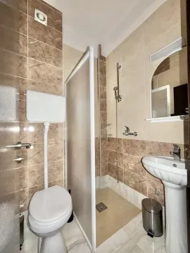 Small tiled bathroom with a shower cabin, washbasin, and toilet. - image 8