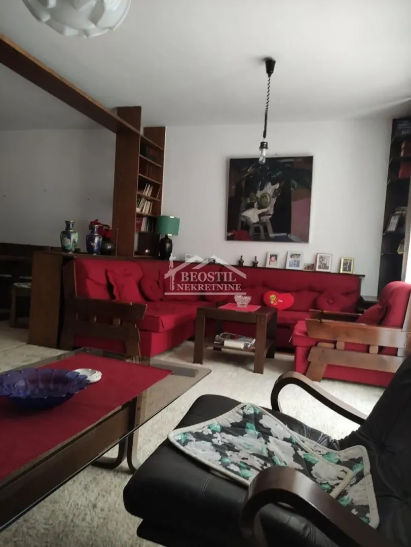 Prostrani dnevni boravak sa crvenim garniturama i drvenim nameštajem.