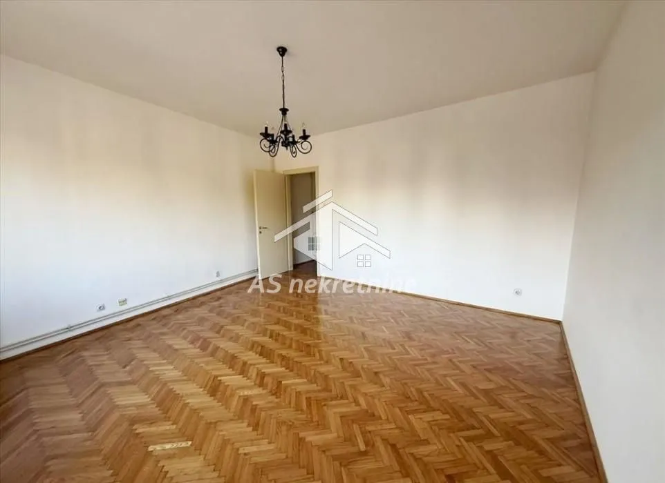 Empty room with hardwood parquet flooring and a chandelier.