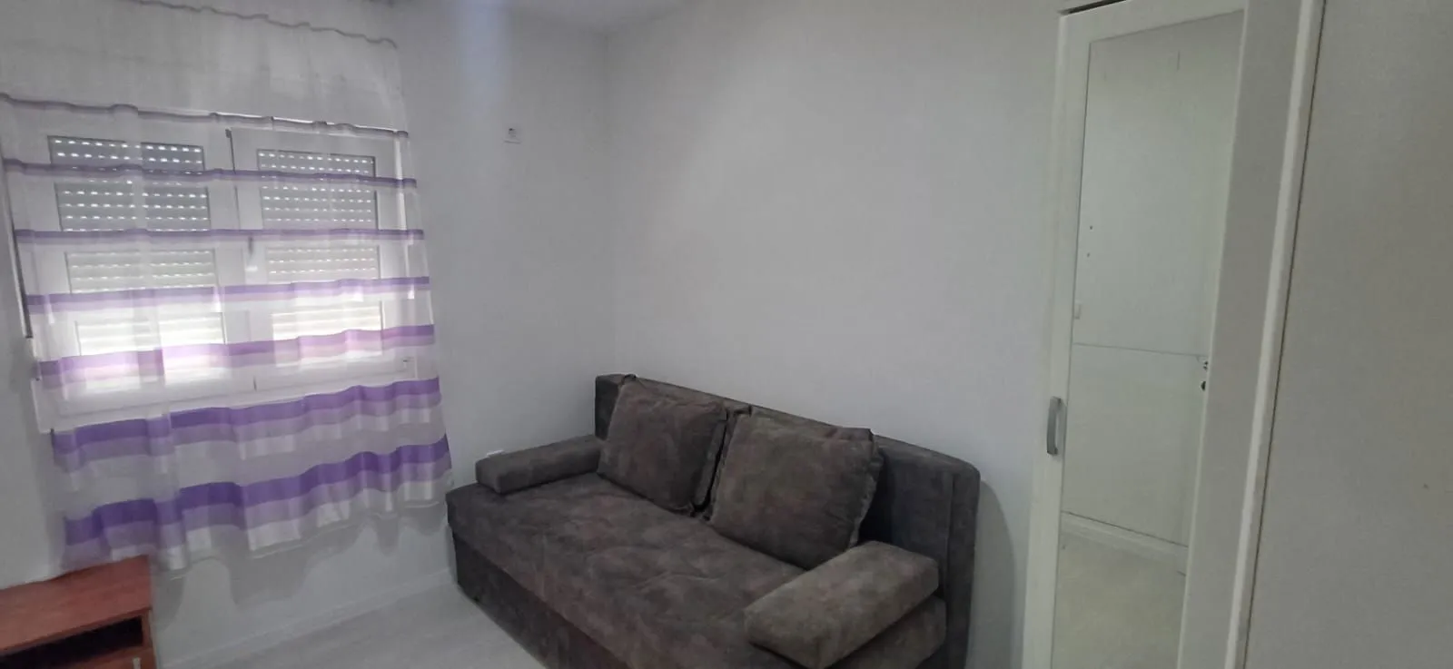 Living room with a grey sofa, wardrobe, and a window with purple curtains.