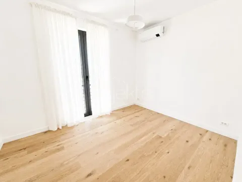 Empty bright room with wooden flooring, an air conditioning unit, and balcony doors with white curtains. - image 10