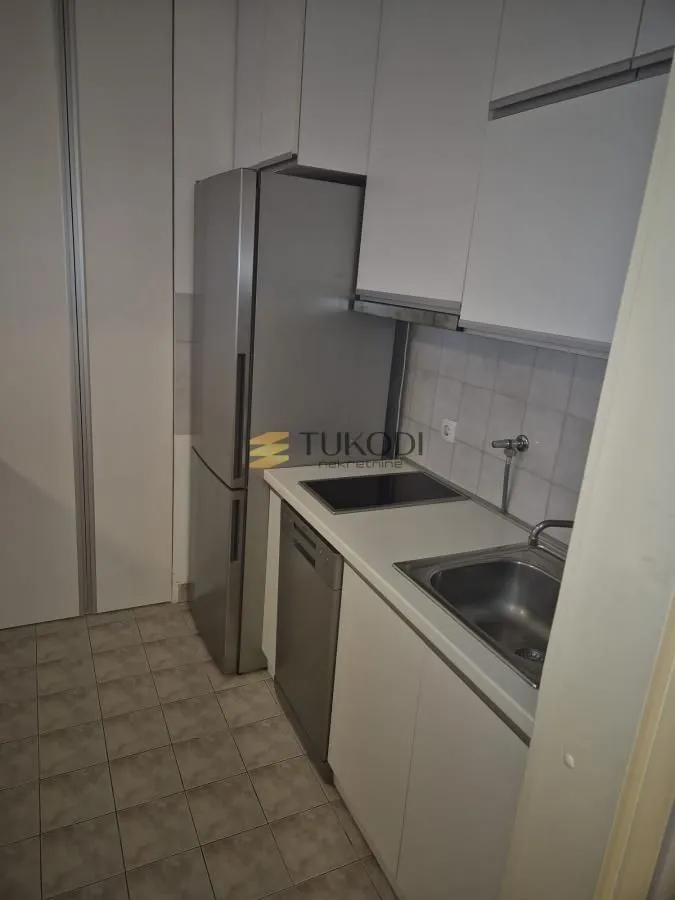 Manja kuhinja sa belim elementima, frižiderom i ugradnom pločom.