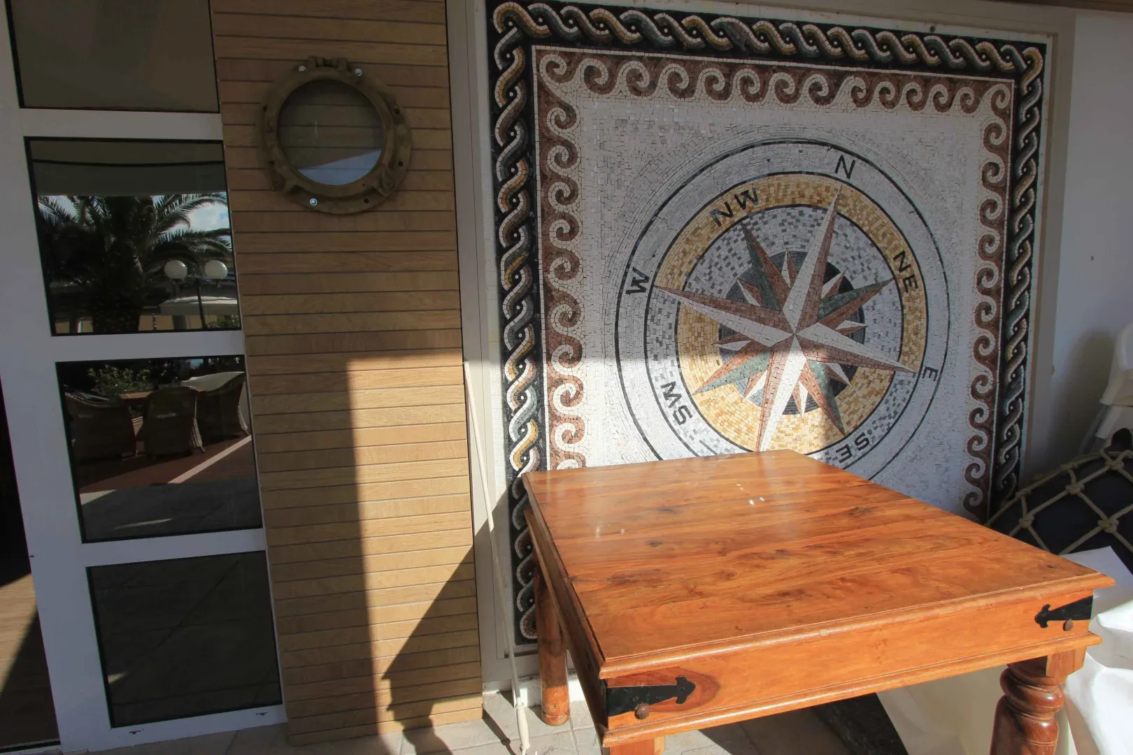 Terrace with a wooden table and a decorative wall mosaic.